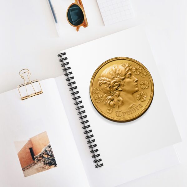 A spiral notebook with a symbol of Tymora, a gold coin, on desk