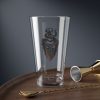 16 oz pint glass with the dnd symbol of Mask, fantasy deity of dungeons and dragons rogues and thieves, on desk