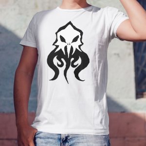The symbol of Deep Duerra, a broken illithid skull, mindflayer, on a white shirt worn by a man against a wall