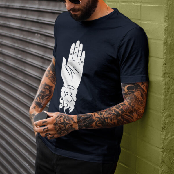 The symbol of Shaundakul, an upright left hand with its wrist trailing away into rippling winds, on a navy blue t-shirt worn by a man leaning against a wall