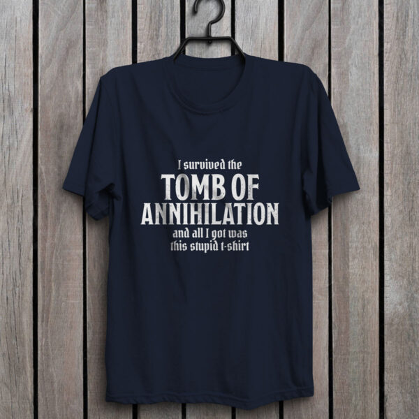 A navy blue D&D shirt telling people that you survived Acererak's Tomb of Annihilation, against a wall