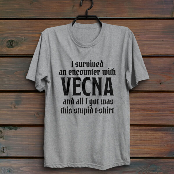 A sport gray D&D shirt telling people that you survived a D&D encounter with the powerful lich Vecna, against a wood wall